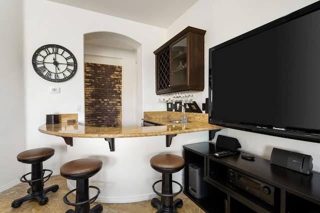 bar featuring dark brown cabinetry, light stone countertops, and light tile patterned floors