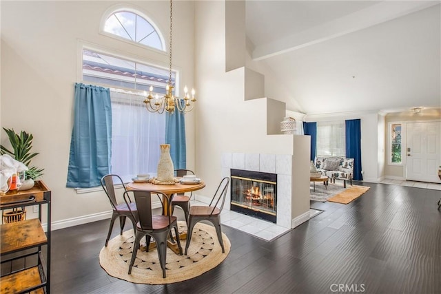 dining room with plenty of natural light, beam ceiling, a tiled fireplace, and a notable chandelier