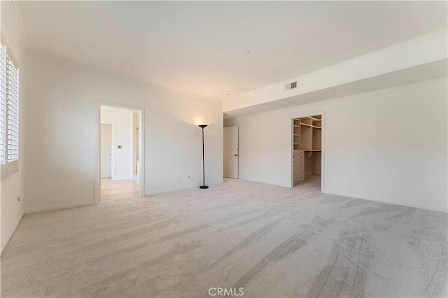 unfurnished bedroom featuring a walk in closet, visible vents, crown molding, and light carpet