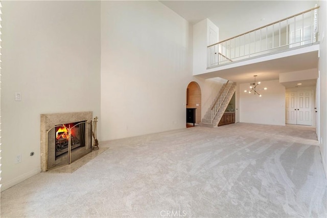 unfurnished living room with a premium fireplace, a high ceiling, carpet, and an inviting chandelier