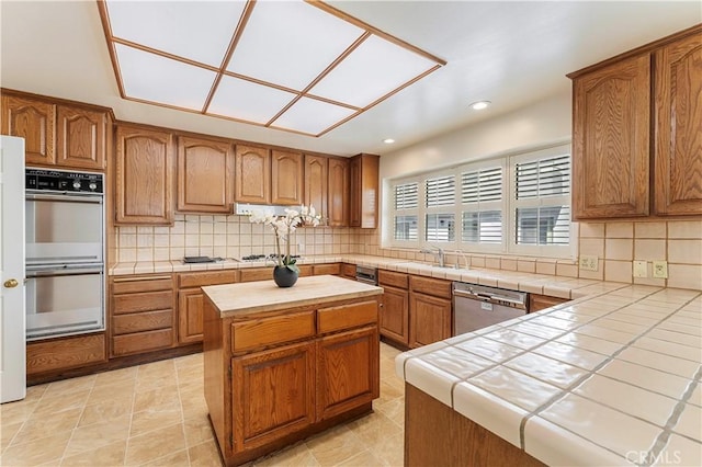 kitchen with tile counters, double oven, dishwasher, and backsplash