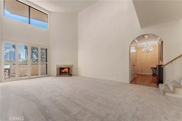 unfurnished living room featuring carpet, stairway, a towering ceiling, arched walkways, and a chandelier