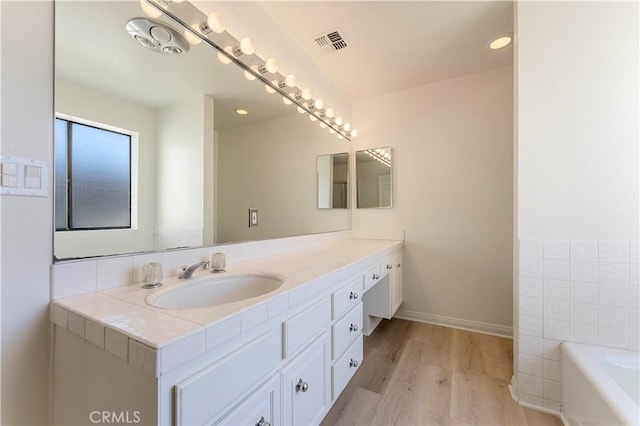 full bath with a tub to relax in, wood finished floors, visible vents, and vanity