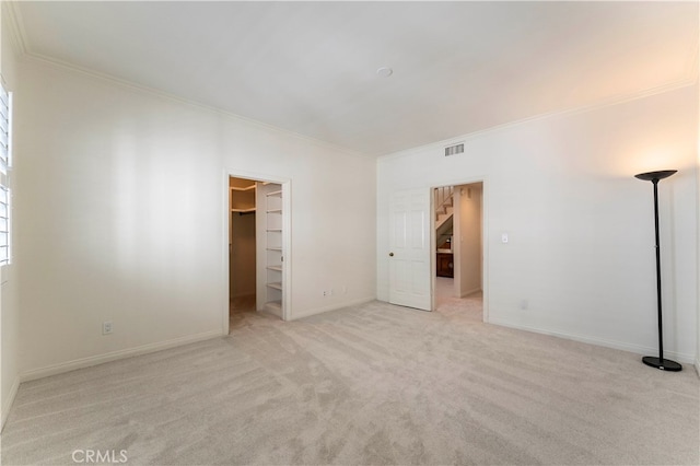 unfurnished bedroom featuring a closet, crown molding, light colored carpet, and a walk in closet