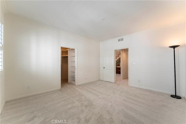 unfurnished bedroom featuring a spacious closet, carpet floors, crown molding, and visible vents