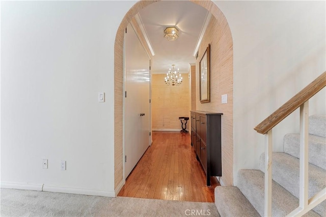 hall with arched walkways, light wood-style floors, a notable chandelier, stairway, and ornamental molding
