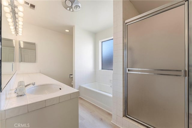 bathroom with a garden tub, wood finished floors, a stall shower, vanity, and recessed lighting