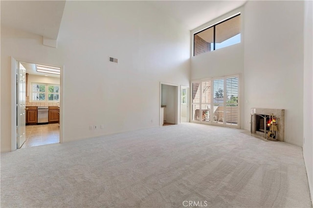 unfurnished living room with a high ceiling, light carpet, visible vents, and a fireplace