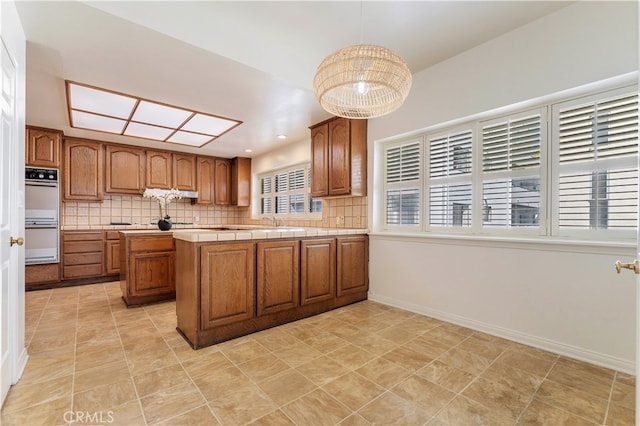 kitchen with decorative light fixtures, tile counters, decorative backsplash, kitchen peninsula, and double oven