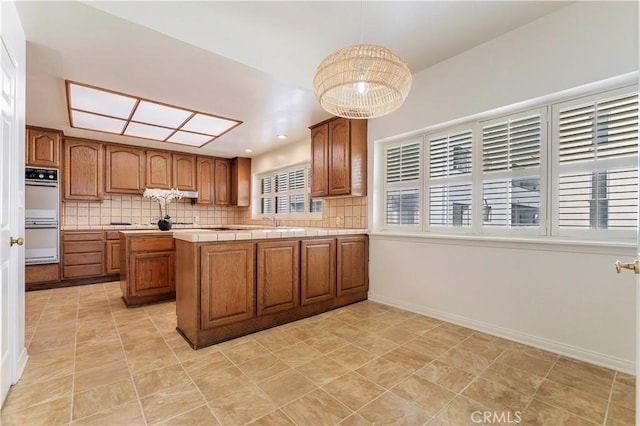 kitchen featuring brown cabinetry, a peninsula, decorative backsplash, and double oven