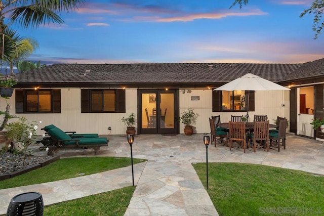 back house at dusk with a lawn and a patio