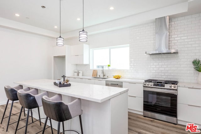 kitchen featuring white cabinets, light hardwood / wood-style flooring, wall chimney range hood, stainless steel appliances, and a center island