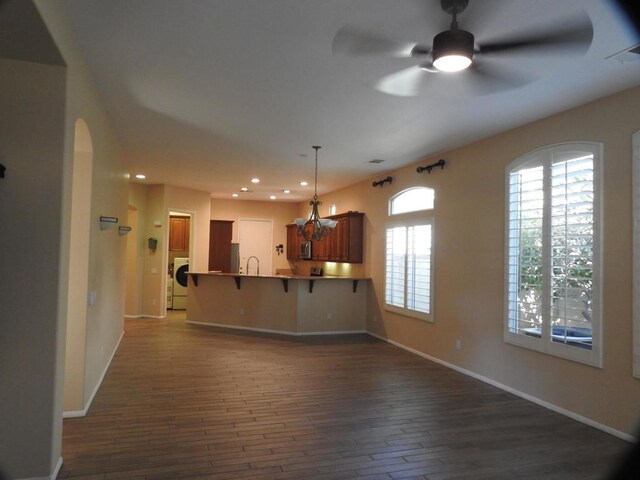 kitchen with washer / dryer, dark hardwood / wood-style floors, kitchen peninsula, hanging light fixtures, and a kitchen breakfast bar