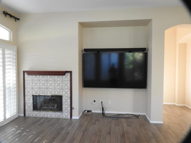 unfurnished living room featuring wood-type flooring and a tiled fireplace