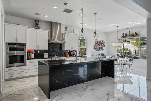 kitchen with white cabinetry, sink, wall chimney exhaust hood, tasteful backsplash, and a large island with sink