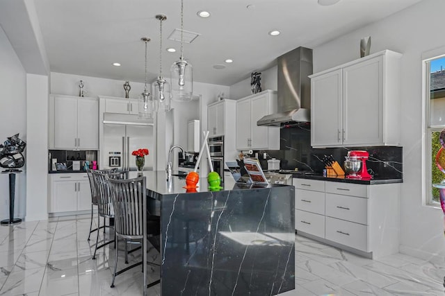 kitchen featuring tasteful backsplash, a kitchen island with sink, wall chimney exhaust hood, and pendant lighting