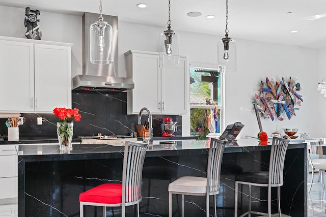 kitchen with white cabinets, a kitchen bar, backsplash, and wall chimney range hood