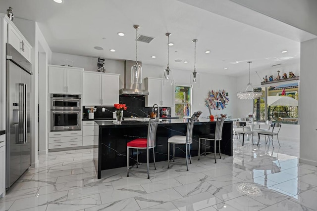 kitchen featuring pendant lighting, stainless steel appliances, white cabinetry, and an island with sink