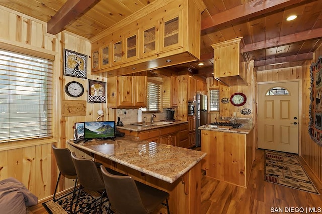 kitchen with wood ceiling, wooden walls, a center island, light stone counters, and beamed ceiling