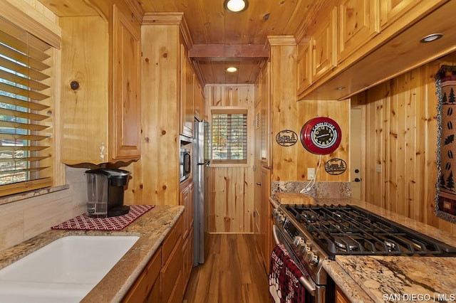 kitchen with light brown cabinets, wooden walls, hardwood / wood-style flooring, stainless steel appliances, and light stone countertops