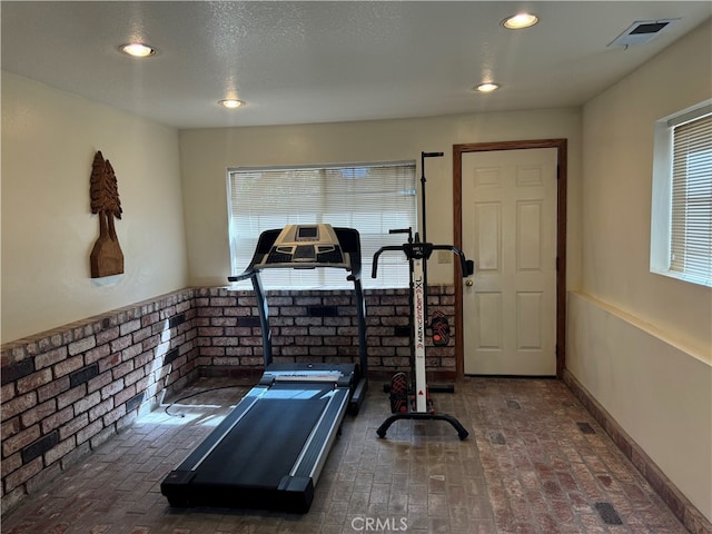 workout room featuring brick wall, a wealth of natural light, and a textured ceiling