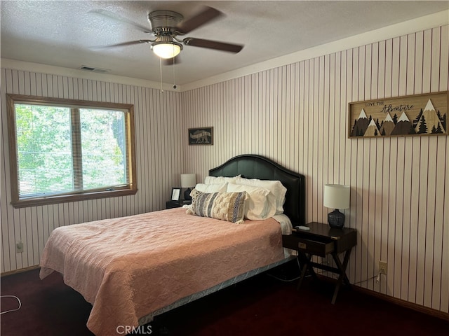 bedroom with wooden walls, ceiling fan, and a textured ceiling