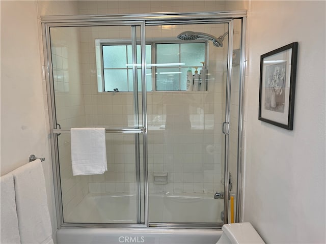 bathroom featuring combined bath / shower with glass door and toilet