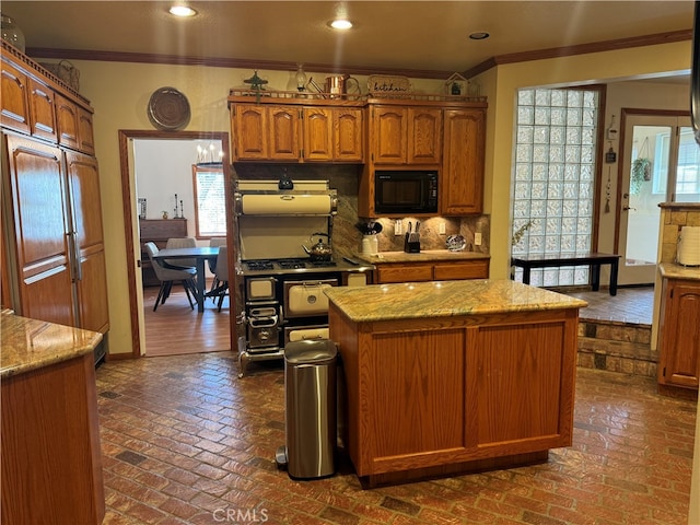 kitchen featuring light stone countertops, a center island, ornamental molding, built in appliances, and backsplash