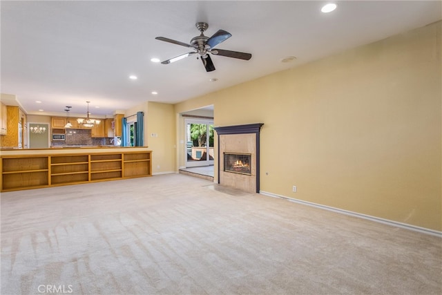 unfurnished living room featuring light colored carpet, ceiling fan with notable chandelier, and a premium fireplace