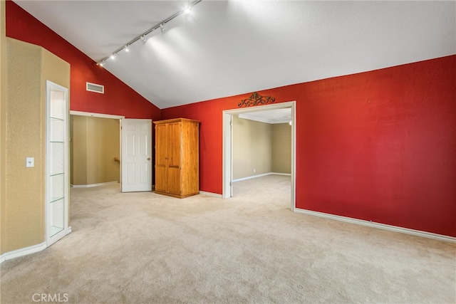 unfurnished bedroom with light carpet, vaulted ceiling, and rail lighting