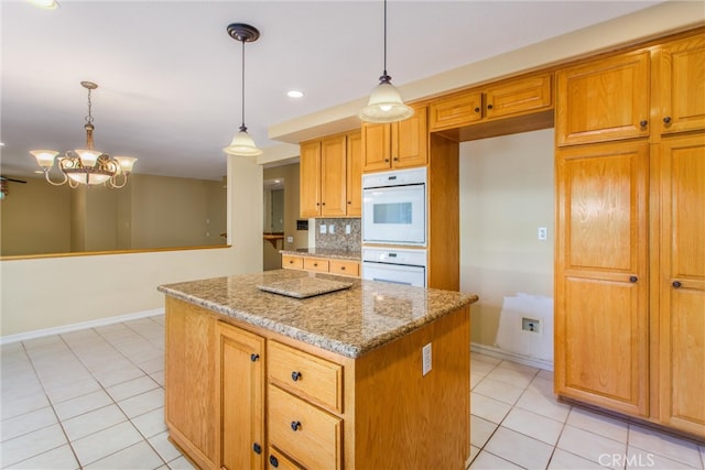 kitchen featuring pendant lighting, a kitchen island, light stone counters, backsplash, and light tile patterned floors