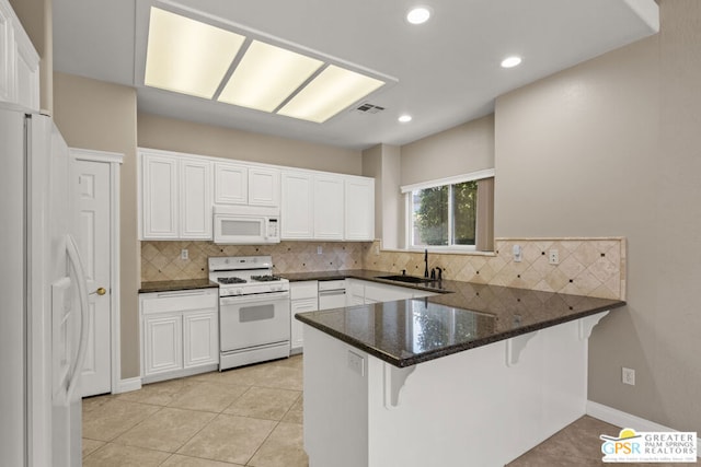 kitchen with white cabinets, sink, kitchen peninsula, white appliances, and a kitchen bar