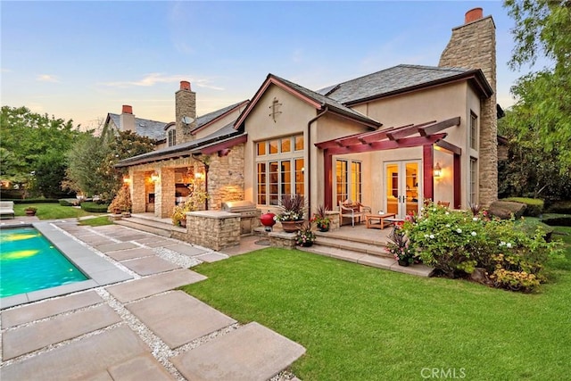 back house at dusk featuring a patio area, a yard, and french doors