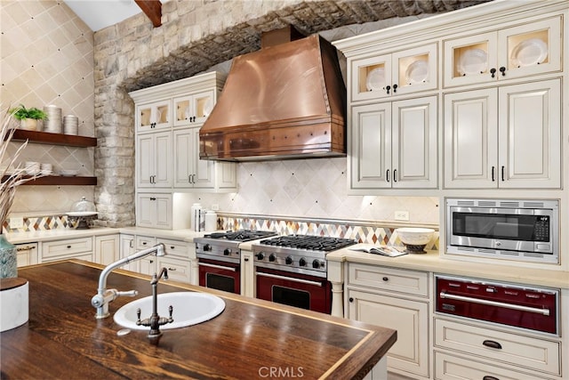 kitchen featuring custom range hood, backsplash, appliances with stainless steel finishes, and sink