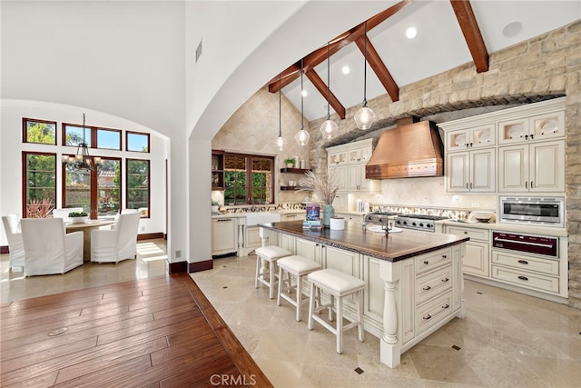 kitchen with beam ceiling, high vaulted ceiling, white dishwasher, a center island with sink, and custom range hood