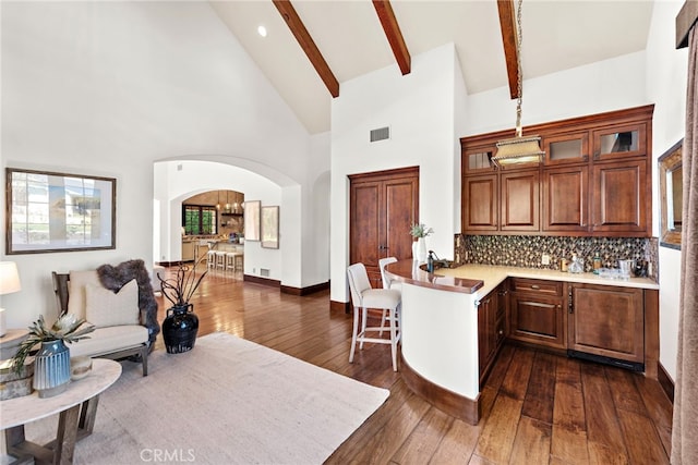 kitchen with kitchen peninsula, decorative backsplash, high vaulted ceiling, beamed ceiling, and dark hardwood / wood-style floors