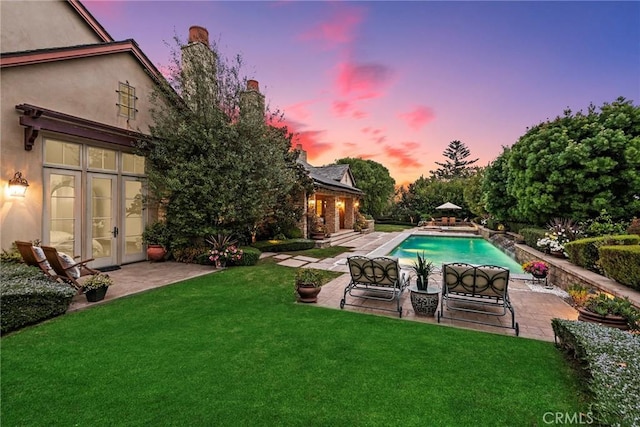 pool at dusk featuring a lawn and a patio area