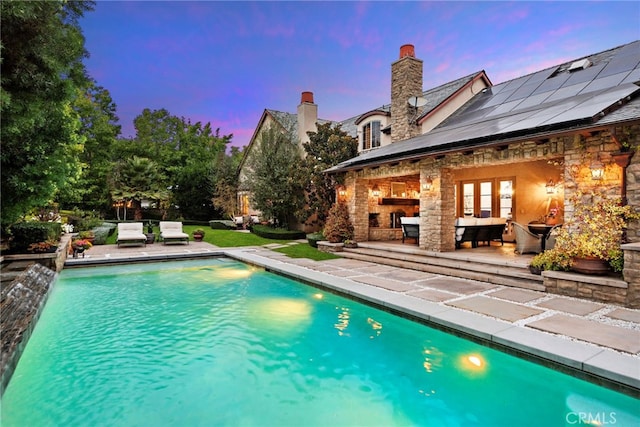 pool at dusk featuring a patio area and exterior fireplace