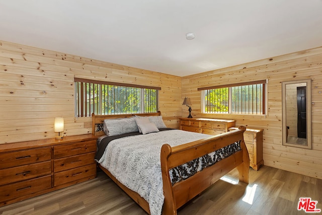 bedroom featuring wood walls, wood-type flooring, and multiple windows