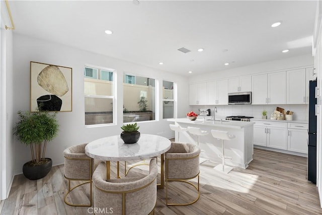 kitchen featuring stainless steel microwave, light countertops, light wood finished floors, and white cabinetry