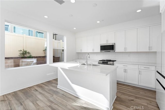 kitchen with sink, stove, white cabinetry, a kitchen island with sink, and light hardwood / wood-style floors