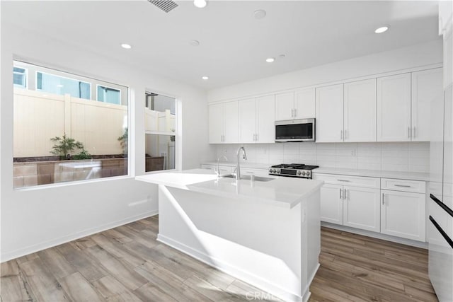 kitchen featuring wood finished floors, a sink, stainless steel microwave, tasteful backsplash, and range