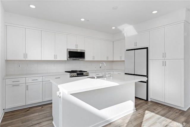 kitchen with fridge, an island with sink, and white cabinets