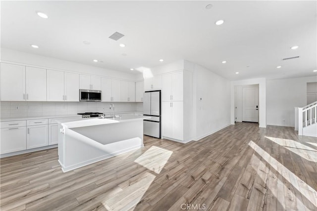 kitchen with white cabinetry, backsplash, white fridge, a kitchen island with sink, and light hardwood / wood-style flooring