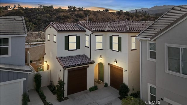 mediterranean / spanish-style home with a tiled roof, a mountain view, fence, a garage, and stucco siding