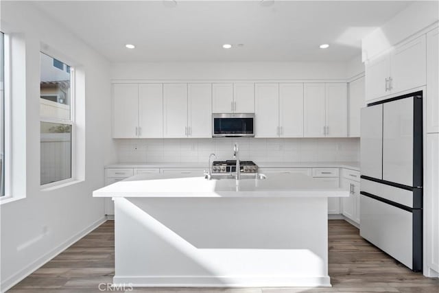 kitchen with white cabinets, backsplash, white refrigerator, hardwood / wood-style flooring, and a center island with sink