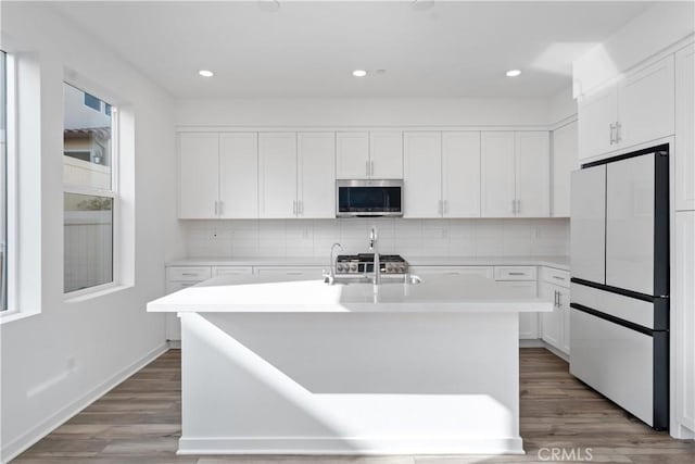 kitchen featuring stainless steel microwave, fridge, backsplash, wood finished floors, and light countertops