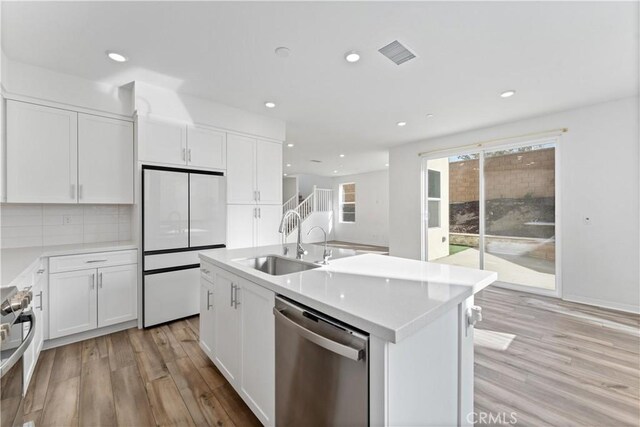 kitchen with sink, light hardwood / wood-style flooring, appliances with stainless steel finishes, a kitchen island with sink, and white cabinets