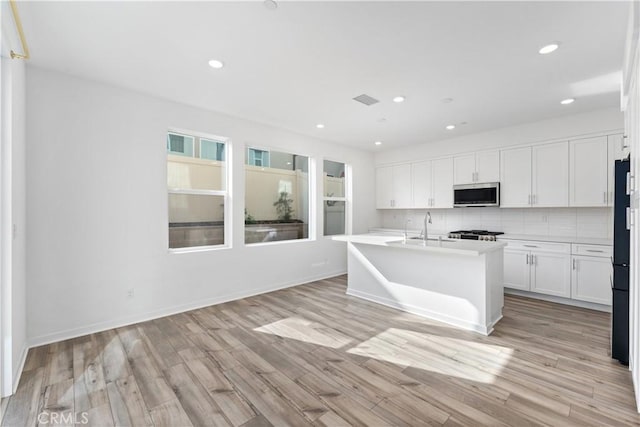 kitchen with a kitchen island with sink, decorative backsplash, light hardwood / wood-style flooring, and white cabinets