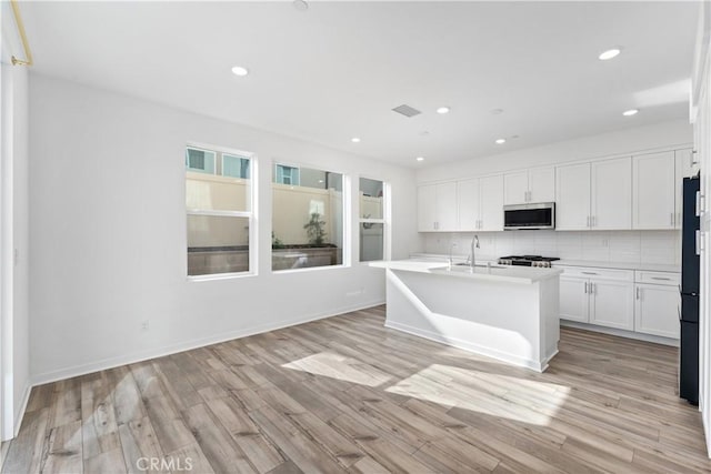 kitchen featuring stainless steel microwave, white cabinetry, a sink, and light countertops